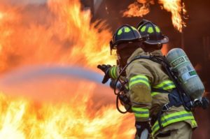 two firefighters spraying water on a house fire