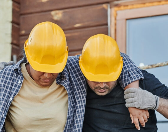One injured construction worker is supported by another.
